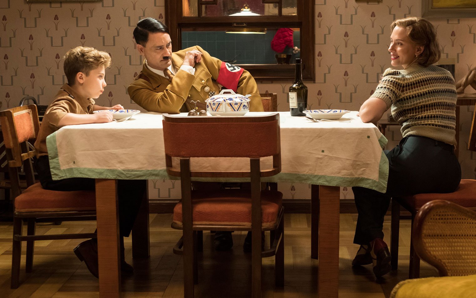 Film still of Jojo Rabbit dinner scene featuring Roman Griffin Davis,  Taika Waititi, and Scarlett Johansson