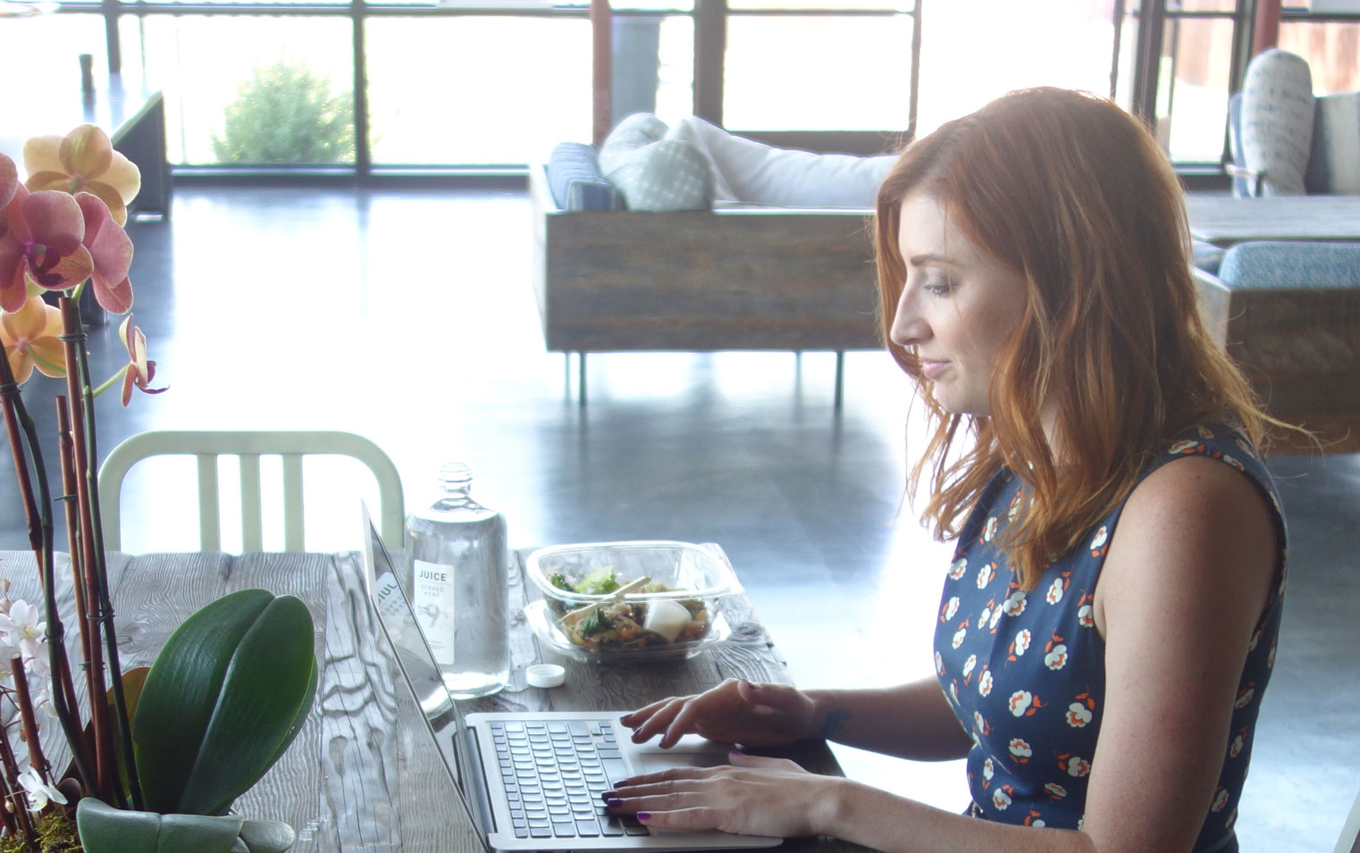 Rachael King, founder of Pod People, seated at table typing on open laptop. 